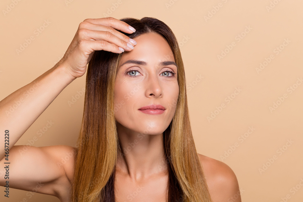 Fototapeta premium Portrait of attractive woman touching clear smooth silky flawless skin lifting solution effect isolated over beige pastel color background