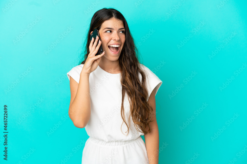 Fototapeta premium Young caucasian woman isolated on blue background keeping a conversation with the mobile phone
