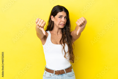 Young caucasian woman isolated on yellow background showing thumb down with two hands