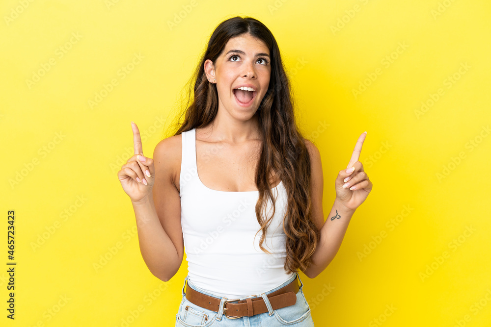 Young caucasian woman isolated on yellow background surprised and pointing up Young caucasian woman isolated on yellow background surprised and pointing up