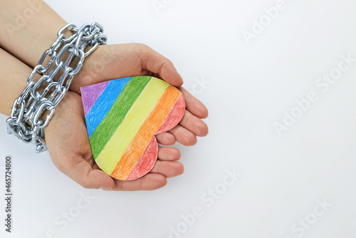 Paper heart painted in LGBT colors in the hands of a woman tied in chains. photo