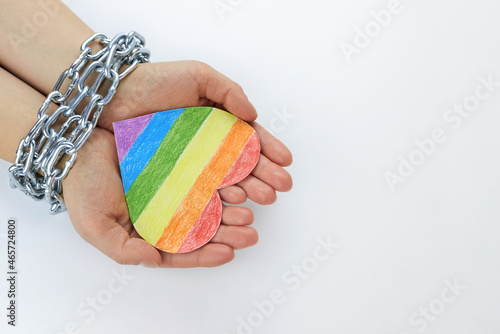Fotografie Paper heart painted in LGBT colors in the hands of a woman tied in chains