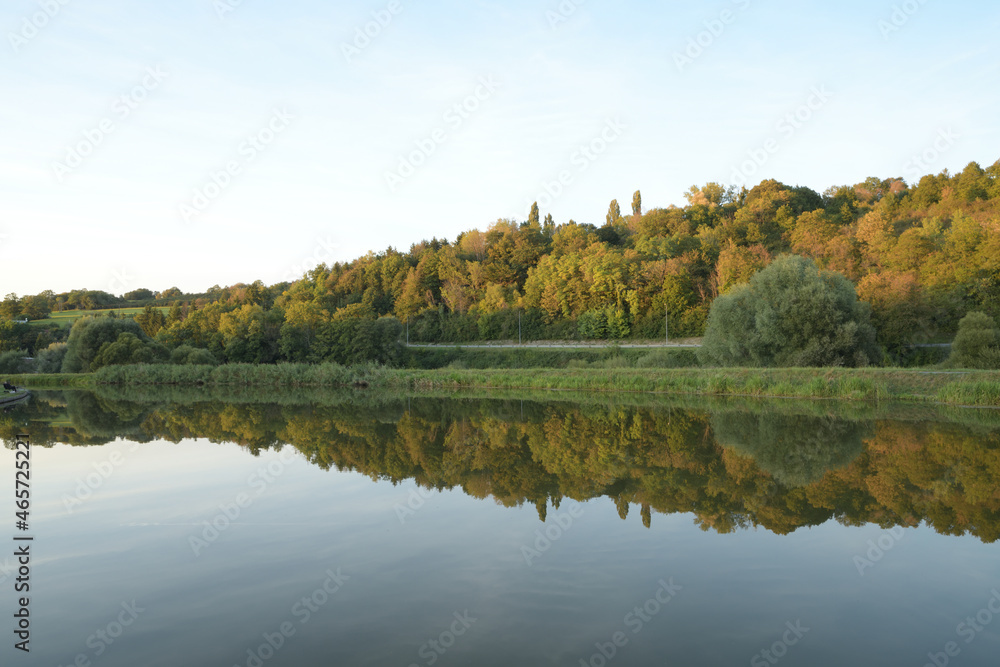 Canal de la Sarre en Moselle, l'automne se dessine à petit pas et les couleurs automnales des arbres se reflètent dans l'eau du canal Canal de la Sarre en Moselle, l'automne se dessine à petit pas et les couleurs automnales des arbres se reflètent dans l'eau du canal