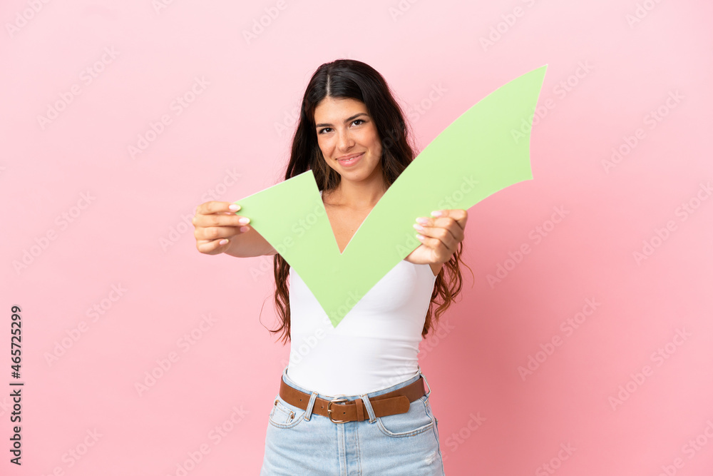 Young caucasian woman isolated on pink background holding a check icon with happy expression Young caucasian woman isolated on pink background holding a check icon with happy expression