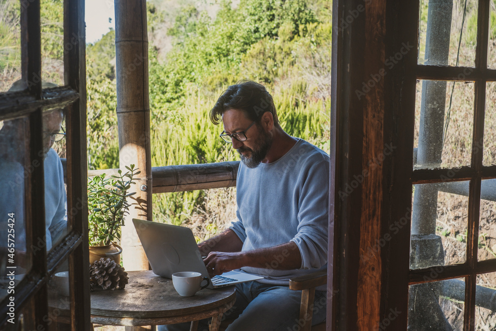 Adult man use laptop computer sitting outdoor at home in alternative office smart working online job activity. Modern people enjoy wireless connection technology to work remote