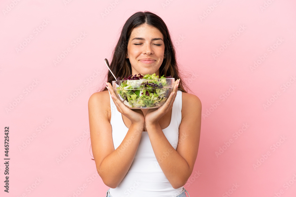 Young caucasian woman isolated on pink background holding a bowl of salad with happy expression