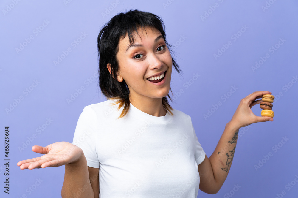 Young Uruguayan woman over isolated purple background holding colorful French macarons with shocked expression Young Uruguayan woman over isolated purple background holding colorful French macarons with shocked expression