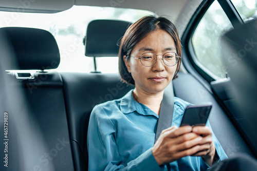 Asian businesswoman on the backseat of a car  using smart phone
