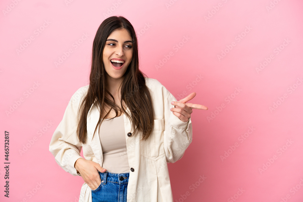 Young caucasian woman isolated on pink background pointing finger to the side and presenting a product Young caucasian woman isolated on pink background pointing finger to the side and presenting a product