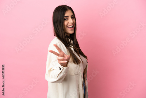 Young caucasian woman isolated on pink background smiling and showing victory sign © luismolinero