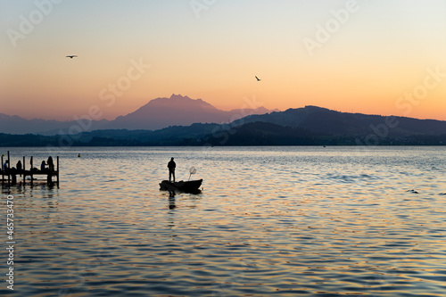 View of Lake Zugersee at sunset, in the Swiss city of Zug. The lake is calm in good weather and the silhouette of a boat with a fisherman. © csbphoto
