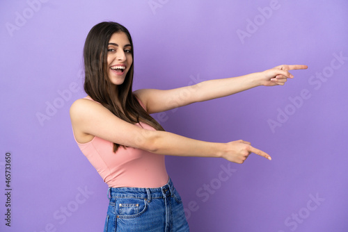 Young caucasian woman isolated on purple background pointing finger to the side and presenting a product
