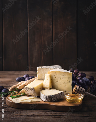 Cheese plate. Assortment of farmers French and Piedmont cheeses served with honey, grape, grissini and rosemary on the wooden rustic background.  Winter and autumn starter or aperitifs photo