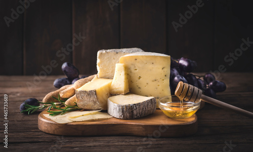 Cheese plate. Assortment of fermers French and Piedmont cheeses served with honey, grape, grissini and rosemary on the wooden rustic background.  Winter and autumn starter or aperitifs photo