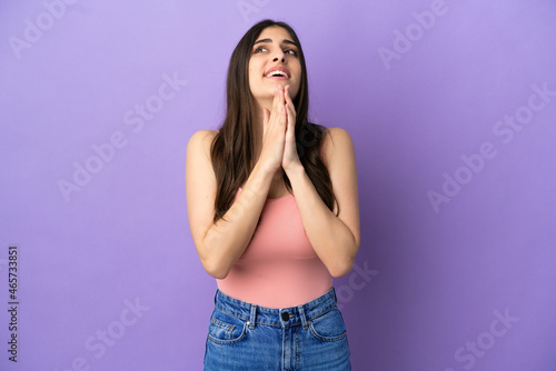 Young caucasian woman isolated on purple background keeps palm together. Person asks for something