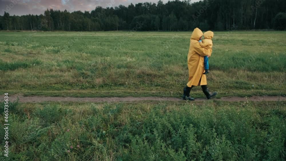 Father walks in the park in the evening with a small child. People in raincoats, cloudy weather. The concept of outdoor walk and atmospheric phenomena Father walks in the park in the evening with a small child. People in raincoats, cloudy weather. The concept of outdoor walk and atmospheric phenomena
