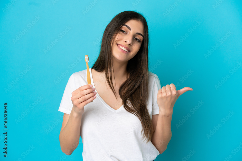 Young caucasian woman brushing teeth isolated on blue background pointing to the side to present a product Young caucasian woman brushing teeth isolated on blue background pointing to the side to present a product