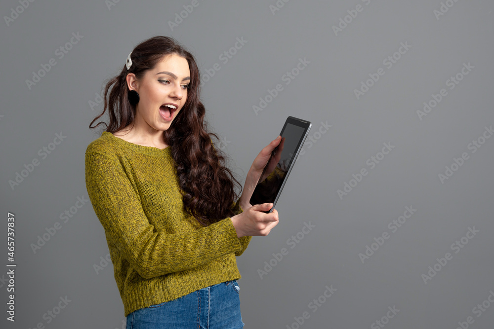 teenage female with long wavy hair having fun with a tablet, isolated on a gray background teenage female with long wavy hair having fun with a tablet, isolated on a gray background