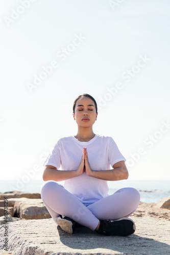 vertical photo of a young asian woman relaxed meditating sitting outdoors with hands together and eyes closed, concept of spirituality and relax