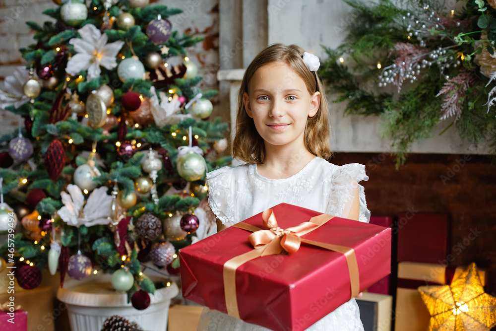 Selective focus. A girl in a white dress with a red gift box close-up in a room decorated with a Christmas tree and a fireplace.