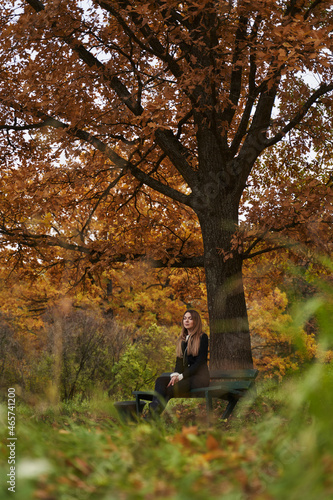 beautiful woman sits in a park under an autumn tree with closed eyes. dreams. meditates. calmness