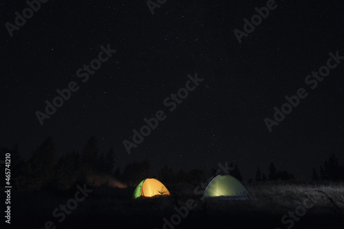 Two color camping tents near forest under sky full of stars at night