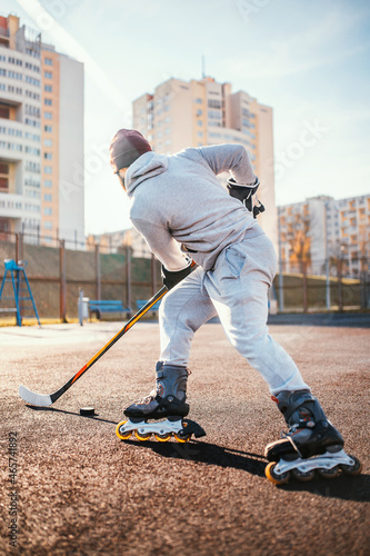 A man practicing hockey outdoors on a rubber surface in sunny weather - roller skating training - turn with a puck photo