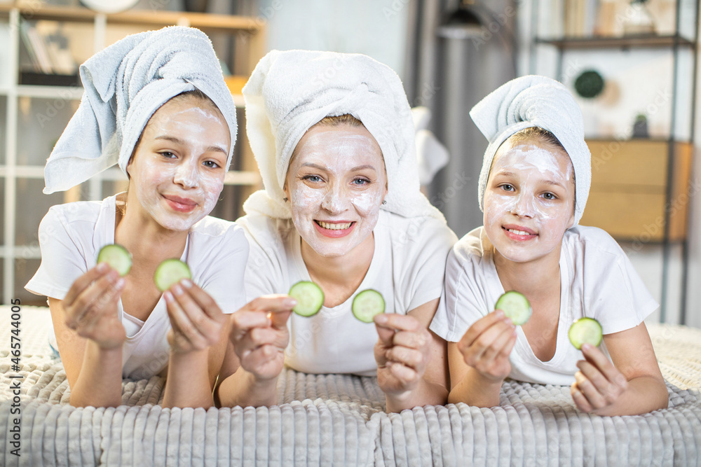 Portrait of happy mature woman lying on sofa with her pretty teen daughters and doing vitamin mask on face. Beauty procedures for healthy and smooth skin. Portrait of happy mature woman lying on sofa with her pretty teen daughters and doing vitamin mask on face. Beauty procedures for healthy and smooth skin.
