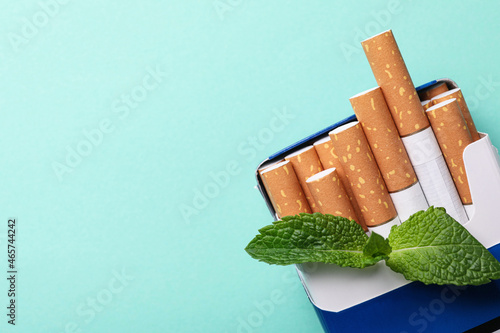 Pack of menthol cigarettes and mint on turquoise background, top view. Space for text