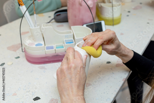 Women's hands wipe a ceramic cup with a sponge. The stage of applying the glaze before firing. Ceramic workshop.