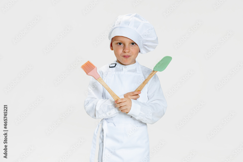 Close-up portrait of little happy boy in white cook uniform and huge chef's hat looking at camera isolated on white studio background. Close-up portrait of little happy boy in white cook uniform and huge chef's hat looking at camera isolated on white studio background.