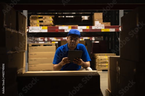 Young worker in blue uniform checklist manage parcel box product in warehouse. Asian man employee using tablet working at store industry. Logistic import export concept. photo