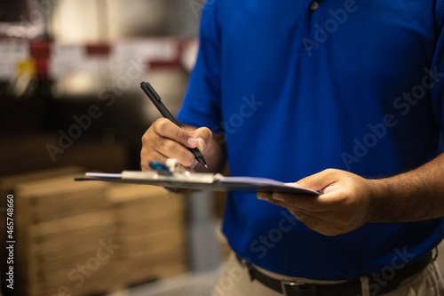 Young worker in blue uniform checklist manage parcel box product in warehouse. Asian man employee holding clipboard working at store industry. Logistic import export concept.