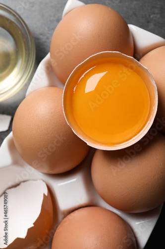 Box of whole and cracked chicken eggs on grey table, flat lay