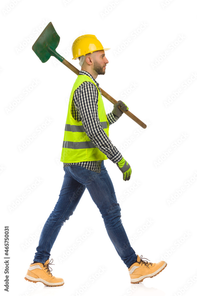 Construction worker is walking with shovel on a shoulder. Side view. Studio shot isolated. Construction worker is walking with shovel on a shoulder. Side view. Studio shot isolated.