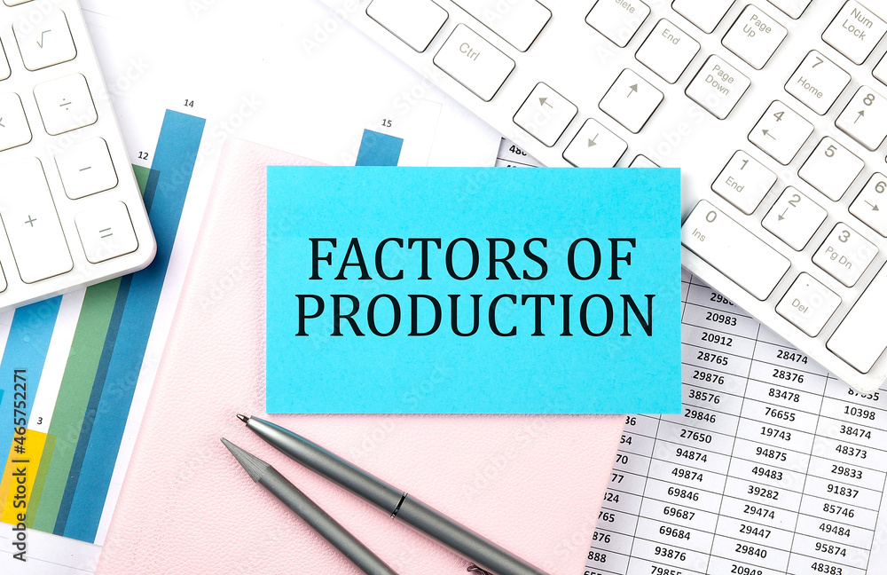 FACTORS OF PRODUCTION text on blue sticker on chart with calculator and keyboard FACTORS OF PRODUCTION text on blue sticker on chart with calculator and keyboard
