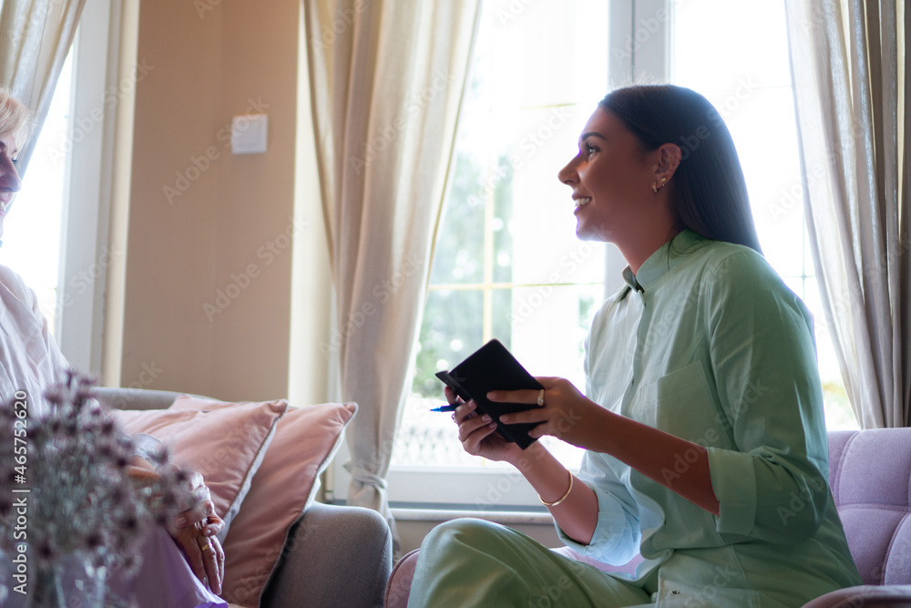 Young female nurse visiting a mature woman at her home, doing a house call visit.
