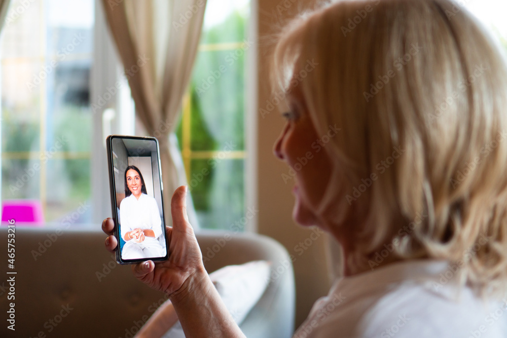 A mature woman is using a mobile phone for online consultation with her doctor in a video call. A mature woman is using a mobile phone for online consultation with her doctor in a video call.