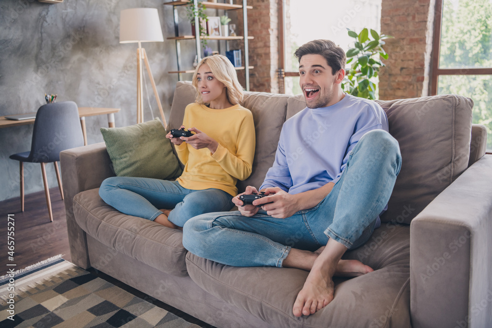 Photo of beautiful excited young lovers dressed casual clothes sitting sofa holding playstation smiling indoors apartment
