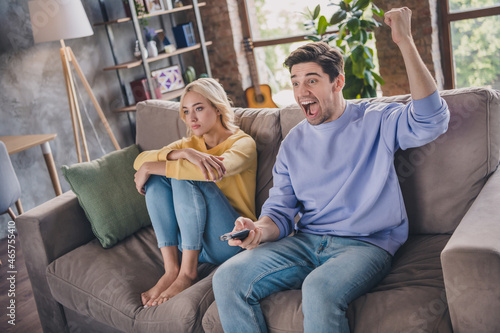 Portrait of attractive cheerful couple sitting on divan watching tv show having fun at home loft industrial interior indoors