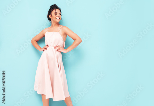 Portrait of young beautiful smiling female in trendy summer dress. Sexy carefree woman posing near blue wall in studio. Positive model having fun indoors. Cheerful and happy