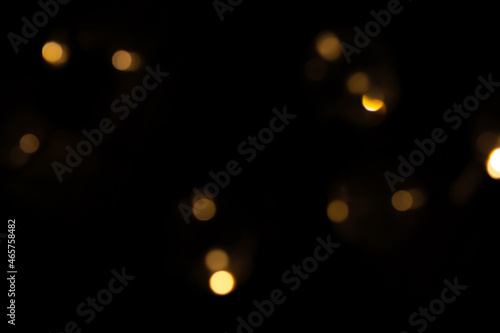 Defocused bokeh lights on black background, an abstract naturally blurred backdrop for Christmas eve or birthday party. Festive light texture. Yellow and red garland in blur. Overlay effect for design