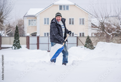 Winter, people and snow problem concept - man digging snow with shovel at yard. Man standing with blue shovel, cleaning.  © T.Den_Team