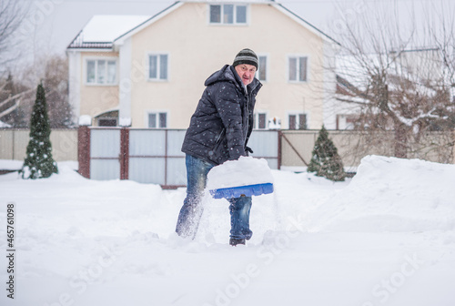 Winter, people and snow problem concept - man digging snow with shovel at yard. Man standing with blue shovel, cleaning. 