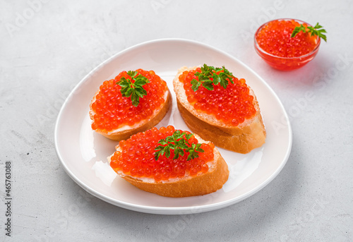 Sandwiches with red caviar in a white plate on a gray background.