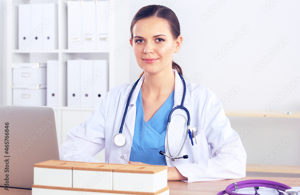 Beautiful young smiling female doctor sitting at the desk and writing. Beautiful young smiling female doctor sitting at the desk and writing.