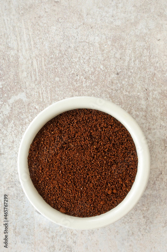 Ground Coffee Beans in a White Ceramic Ramekin on Sand Stone Background