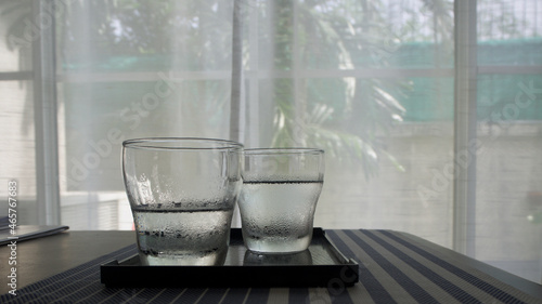 Glass of water; fresh come with water drop around the glass, are on the table that take a garden view.