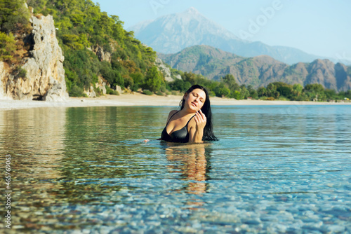 A girl with long dark hair swims in the sea on a beautiful deserted beach with green mountains along the banks. Turkey.