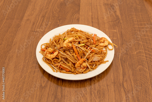 Asian recipe of noodles sautéed with vegetables and prawns with soy sauce on wooden table